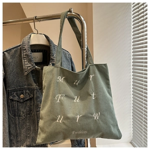 Macro detail of bean green corduroy tote bag featuring white embroidered future lettering