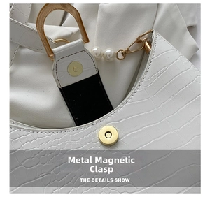 Macro view of gold magnetic clasp and pearl chain on white faux crocodile leather bag