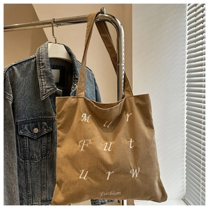 Close-up of brown corduroy tote bag with white art lettering and Fashion embroidery