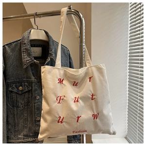 Detail of off-white corduroy tote bag with red letter embroidery on a metal hanger