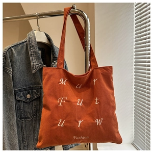 Detailed view of the caramel corduroy tote bag featuring white letter embroidery and texture
