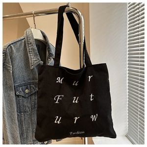 Detail of black corduroy tote bag showing white letter embroidery and soft texture