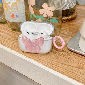 Close-up of clear AirPods Pro case featuring a pink crystal butterfly and metal ring