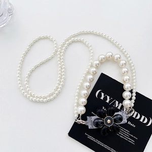 Detail of beaded pearl crossbody strap with black floral charm and secure clips