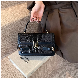 Detail of black crocodile embossed shoulder bag with shiny texture and gold metal clasp