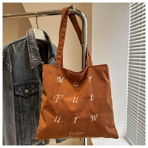 Detailed texture of dark brown corduroy tote bag with white embroidered letters