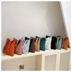 Detailed display of corduroy tote bags in multiple colors with embroidered letter detail