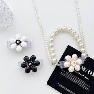 Close-up of floral phone case clips and elegant pearl chain necklace on white surface