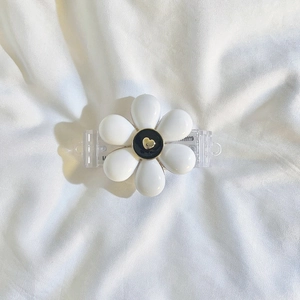 Macro view of white flower hair claw clip with black center and golden heart on fabric