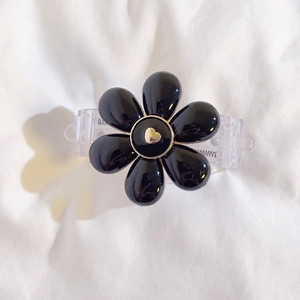 Detail of a black floral hair claw with a gold heart center on a white textured fabric
