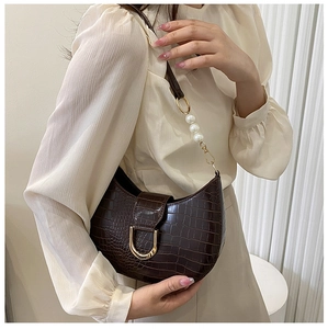 Detail of dark brown crocodile embossed crescent bag with gold D-buckle and pearl strap