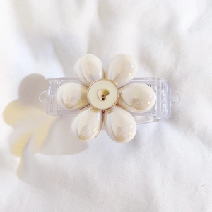 Detailed close-up of cream resin flower hair clip with a gold heart center on white fabric