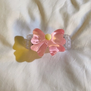 Detailed view of a pink translucent bow clip with yellow bead on white fabric