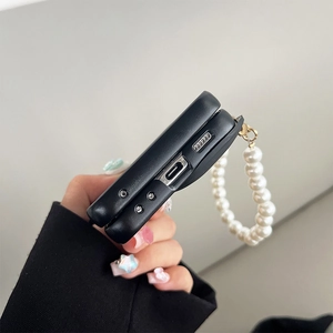 Detail of black folding phone case featuring a white faux pearl hand strap and gold hardware