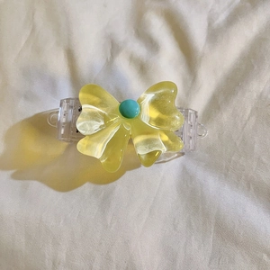 Detail of yellow bow hair claw clip with turquoise bead on soft fabric background
