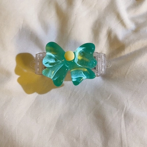 Detail of emerald green translucent bow clip with yellow bead on white fabric