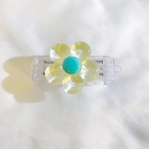 Detail of yellow-green resin flower clip with blue center on white fabric background