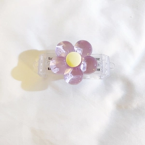 Detailed view of a purple resin flower charm with yellow core on a clear plastic base