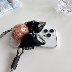 Detail of white phone case with large black bow, plush charm, and braided crossbody strap
