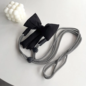 Detail of adjustable black and white braided crossbody strap with 3D cotton bow accent