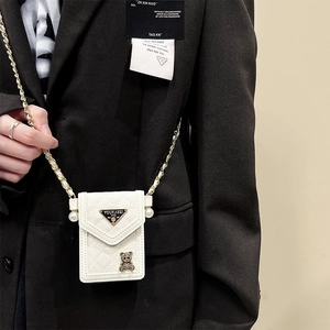 Detail of white quilted phone case bag with pearl chain and golden bear charm