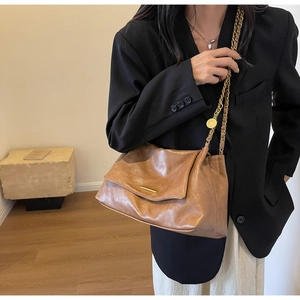Detail of vintage brown leather tote bag showing gold chain strap and textured flap closure