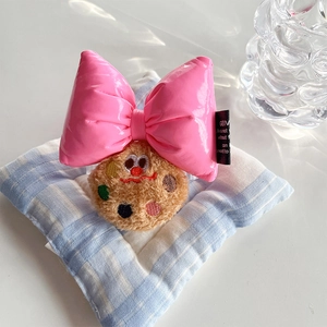 Close-up of pink patent leather bow and plush chocolate cookie charm on a phone clip