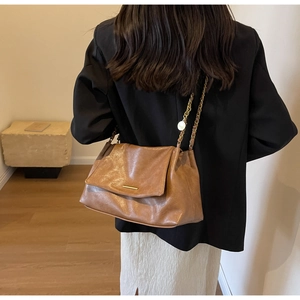 Detail of brown vintage faux leather crossbody bag with gold chain strap on black blazer