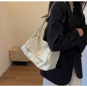 Detail of cream PU leather bag featuring gold metal trim and woven chain strap on black blazer