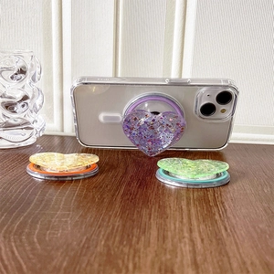 Detail of sequin heart magnetic phone grips in purple, gold, and green on white wood surface
