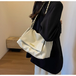 Detail of off-white tote bag showing glossy texture and gold chain strap on shoulder