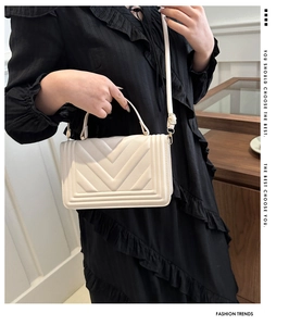 Detail view of cream PU crossbody bag with V-quilt stitching and chain strap on model