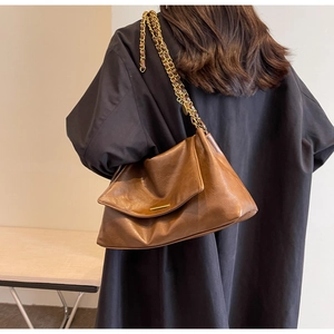 Detail of vintage brown tote bag with glossy texture and gold chain strap on model