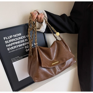 Detail of dark brown glossy leather tote featuring gold metal chain and minimalist hardware