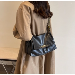 Detail shot of a large black leather shoulder bag with a gold metal bar and chain strap