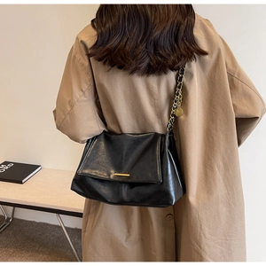 Detail of minimalist black crossbody bag with gold hardware and chain strap on a trench coat