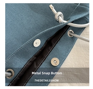 Macro detail of the silver magnetic snap closure on the blue canvas tote bag