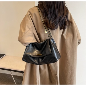 Detail of a black glossy leather tote bag with gold chain strap on a trench coat