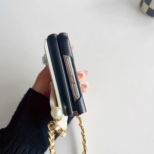 Detail of folding phone case with white leather texture, gold chain and pearl accent