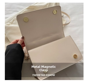 Detail of the golden magnetic buckle closures on a beige textured rectangular bag