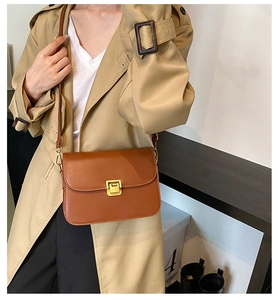 Detail of a brown leather crossbody bag with a gold buckle worn by a model in a studio