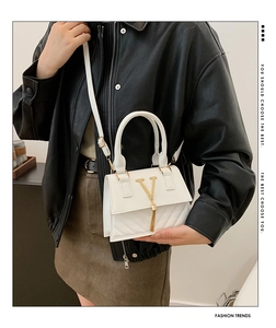 Detail of white quilted crossbody bag with golden V-logo tassel on stylish black leather jacket