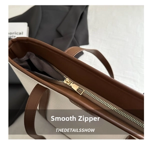 Close-up of smooth gold metal zipper on a beige and brown leather tote bag detail