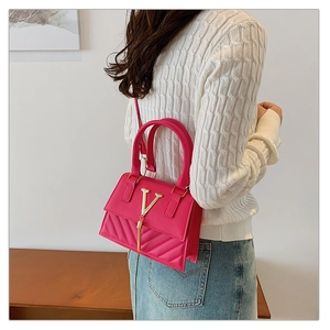 Detail of fuchsia quilted handbag featuring gold V-clasp and chain tassel on model