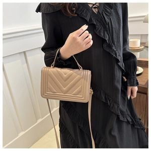 Detailed close-up of light beige crossbody bag with textured V-shape quilted pattern