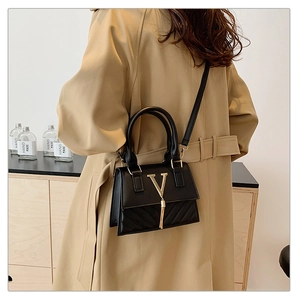 Detail of a black crossbody bag with gold V logo and tassels worn with a trench coat