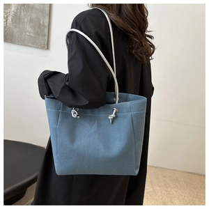 Detail of blue canvas tote bag featuring metallic rope handles and fabric texture details