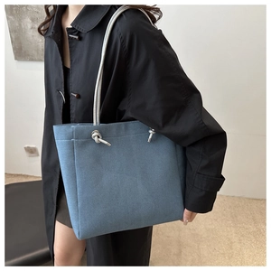 Detail of blue denim tote bag with thick woven rope handles and silver eyelets on a model