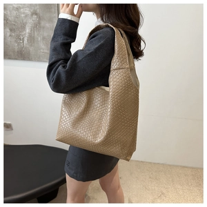 Detailed view of beige woven tote bag with Intrecciato texture worn on the shoulder