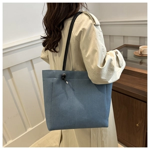 Close-up of light blue canvas tote bag with black rope knot detail and metal accents